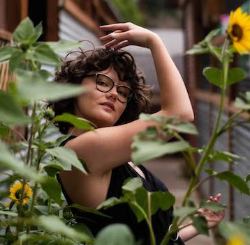 Gretchen Venema behind sunflowers with her arm framing her face